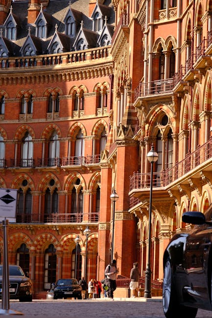 A spacious indoor area of King's Cross railway station featuring a modern, intricate lattice ceiling structure illuminated with purple and white lighting. The high, curved ceiling spans across the station, supported by large white beams forming a web-like pattern. Below, there are ticketing and information displays, digital screens, and a variety of travelers walking, some carrying luggage or boxes in a house removals context. The station's brick walls and large windows are visible to the right, contrasting with the contemporary ceiling design. The environment is lively with groups of people moving through the space, and the lighting highlights the architectural details. This indoor setting illustrates the flow of people during home relocation or furniture transport activities, where clear pathways and organized areas facilitate efficient packing and moving processes, supported by services like Man with Van Kings Cross.